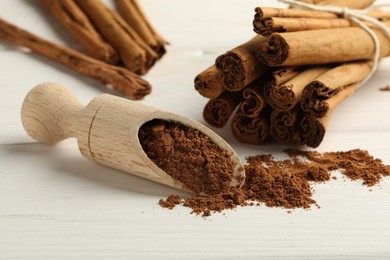 Photo of Dry aromatic cinnamon sticks, powder and scoop on white wooden table, closeup