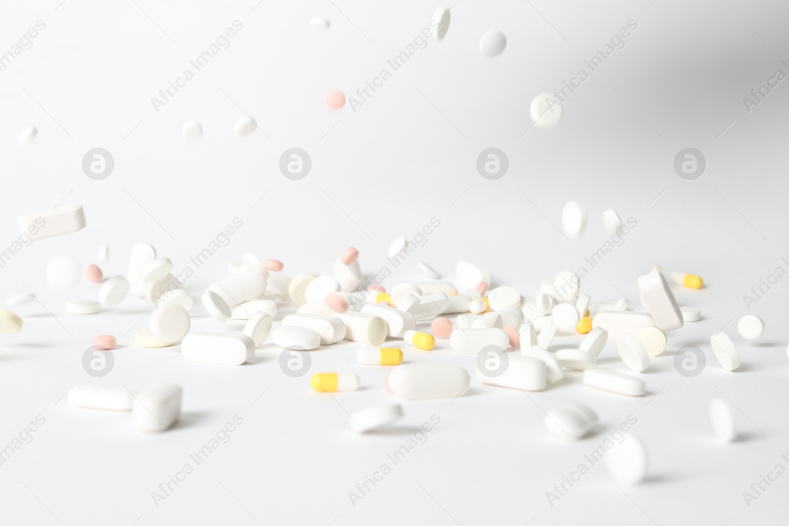 Photo of Different pills falling on table against white background