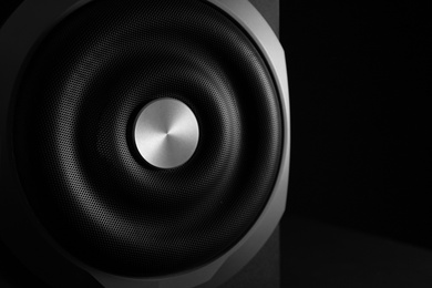 Photo of Closeup view of modern subwoofer on black background, space for text. Powerful audio speaker