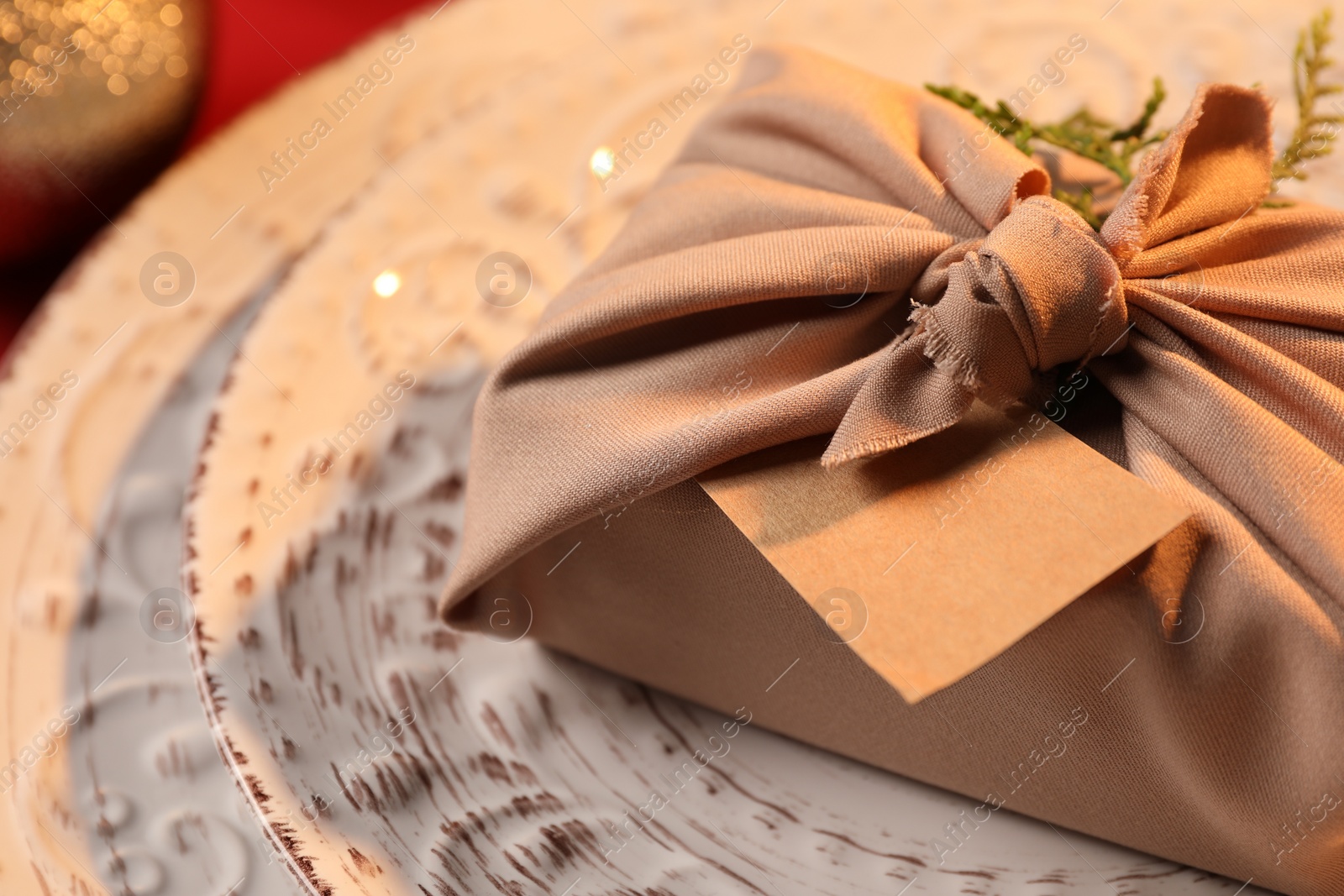 Photo of Furoshiki technique. Gift packed in beige fabric, with blank card on plate, closeup