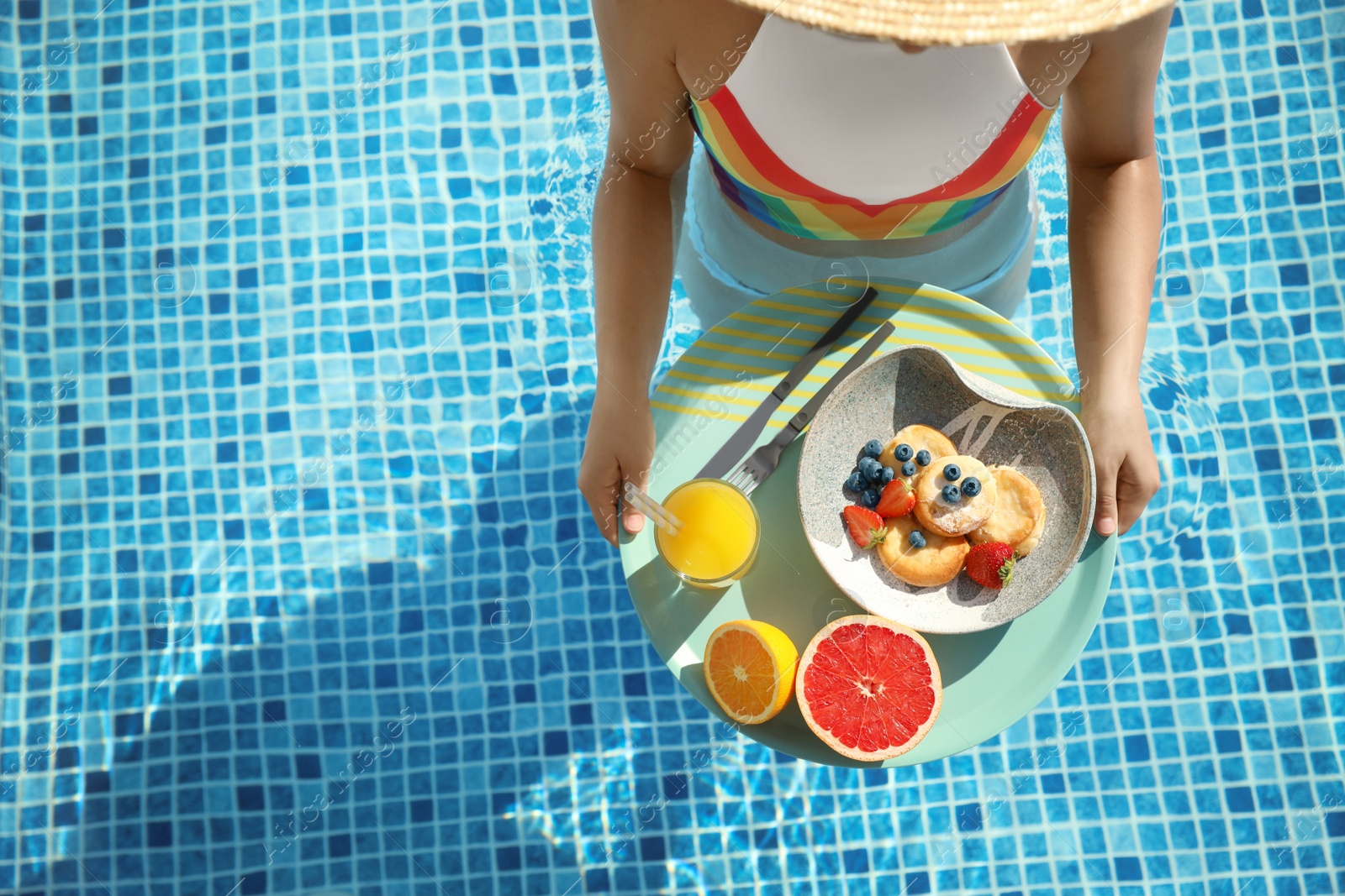 Photo of Young woman with delicious breakfast on tray in swimming pool, top view. Space for text