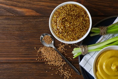 Delicious whole grain mustard, seeds and fresh green onion on wooden table, flat lay