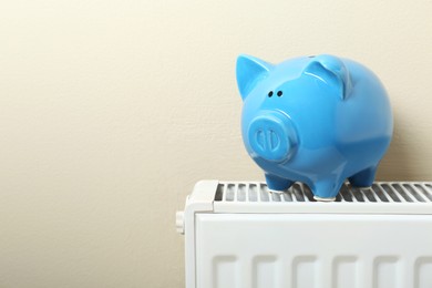 Photo of Piggy bank on heating radiator near beige wall. Space for text