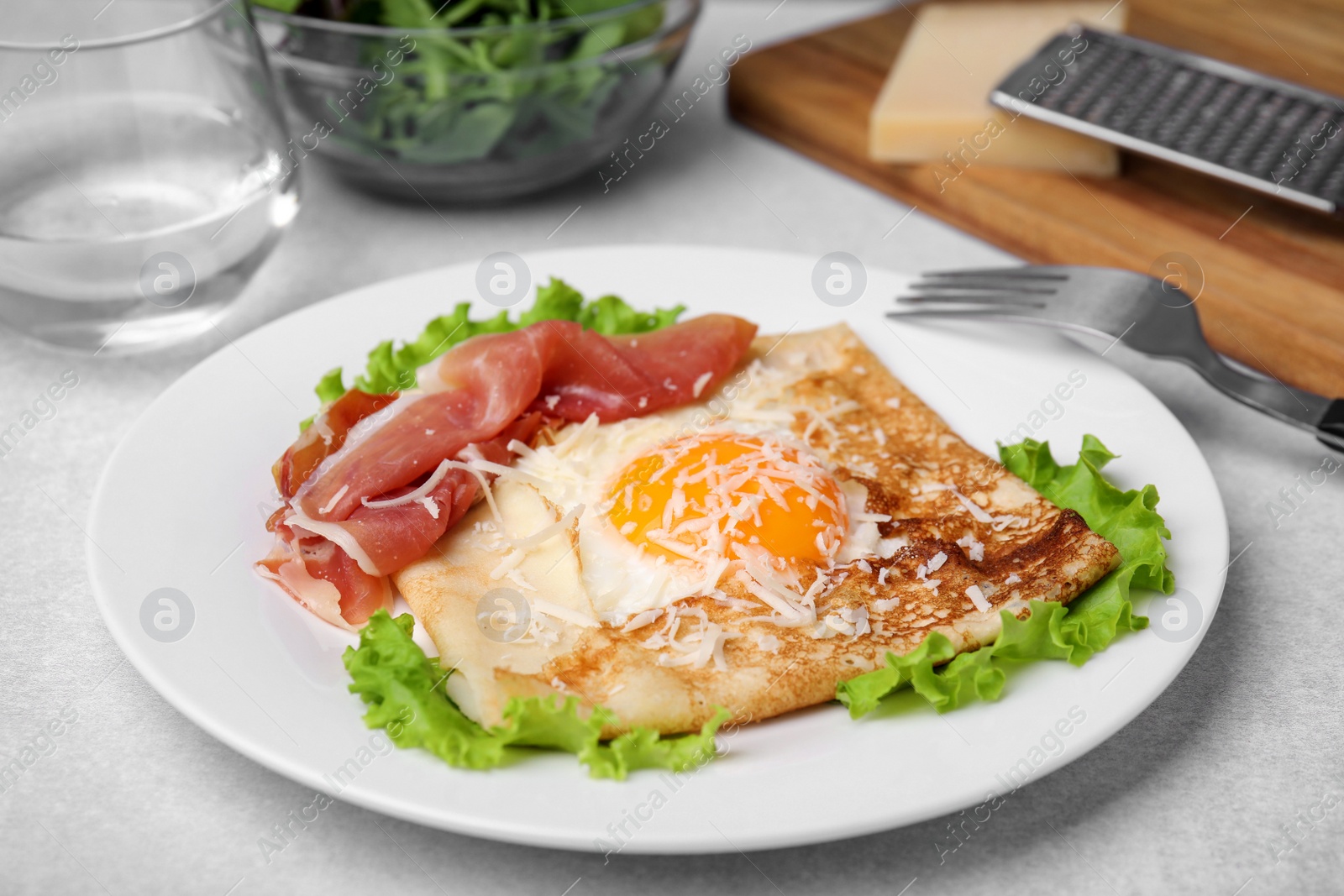Photo of Delicious crepe with egg served on light gray table. Breton galette
