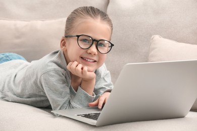 Photo of Portrait of little girl wearing glasses with laptop on sofa