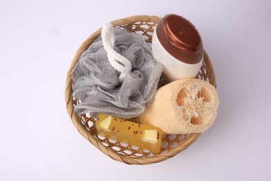 Wicker basket with shower puff, loofah sponge and cosmetic products on white background, top view