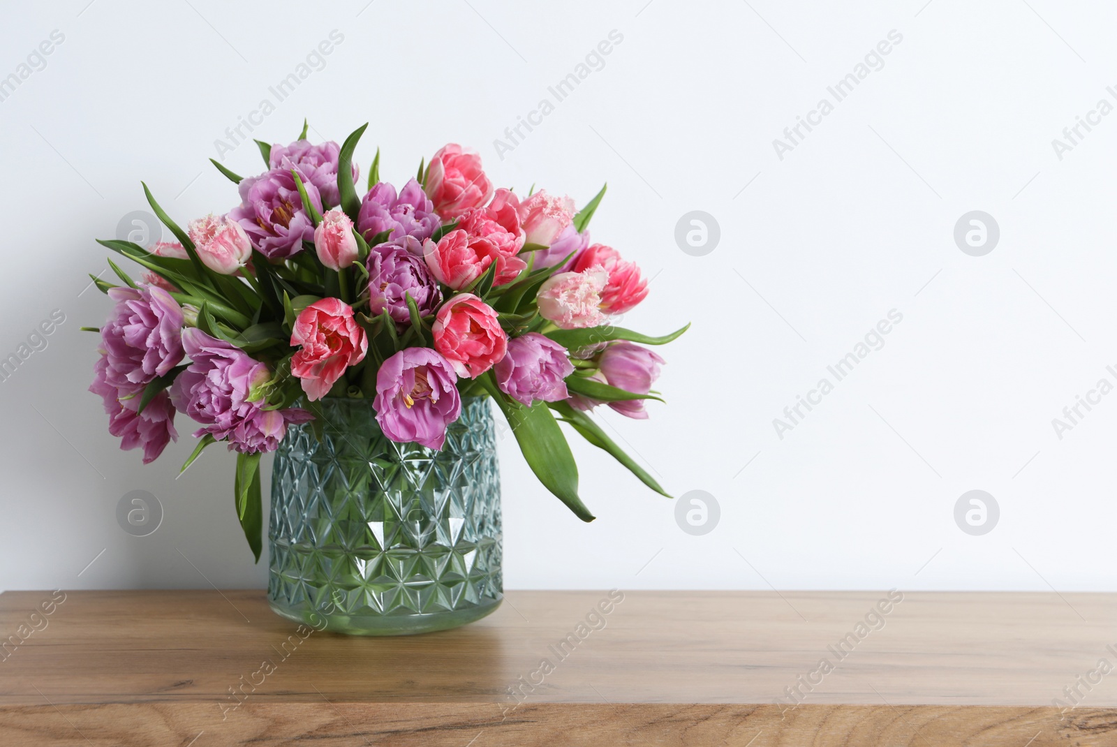 Photo of Beautiful bouquet of colorful tulip flowers on wooden table near white wall. Space for text