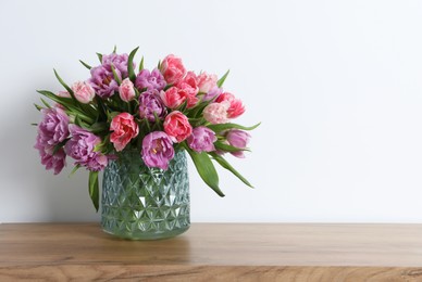 Beautiful bouquet of colorful tulip flowers on wooden table near white wall. Space for text