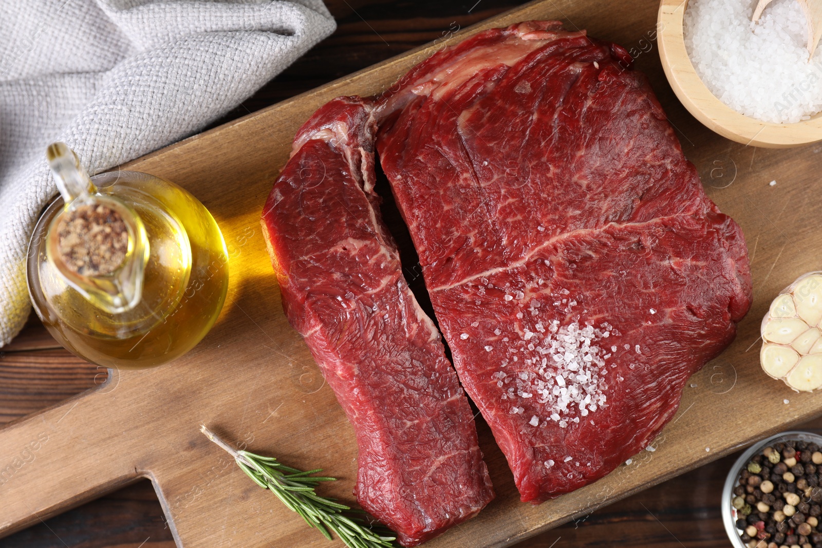 Photo of Fresh raw beef cuts with oil and spices on wooden table, top view