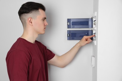 Photo of Young handyman pressing switch on electrical panel board indoors