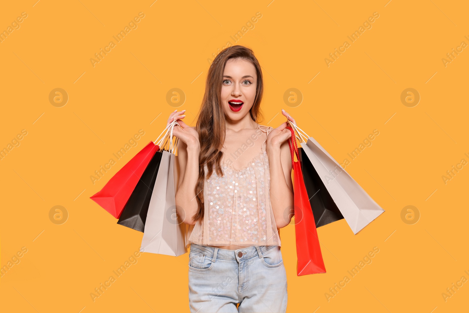 Photo of Excited young woman with shopping bags on orange background