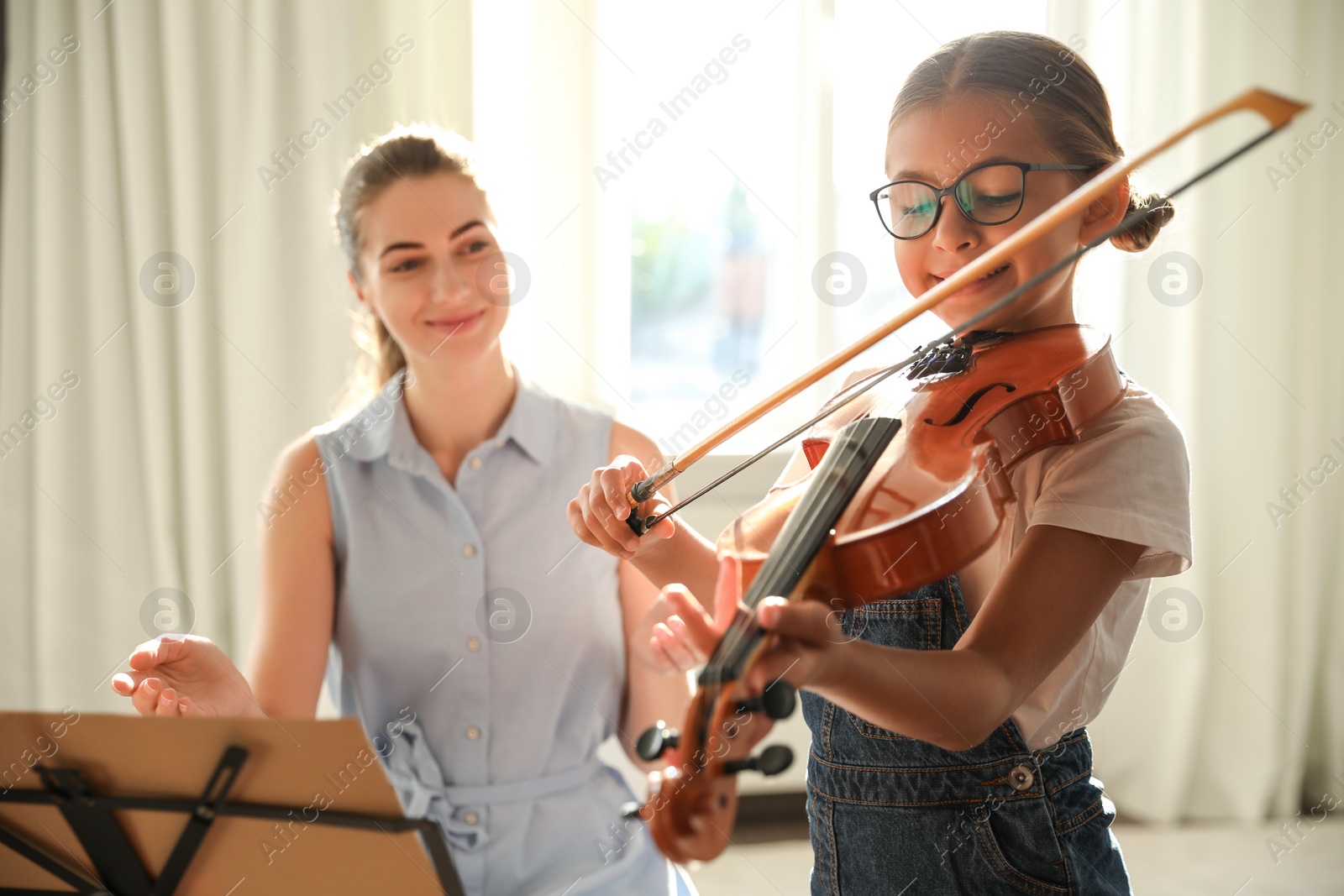 Photo of Young woman teaching little girl to play violin indoors