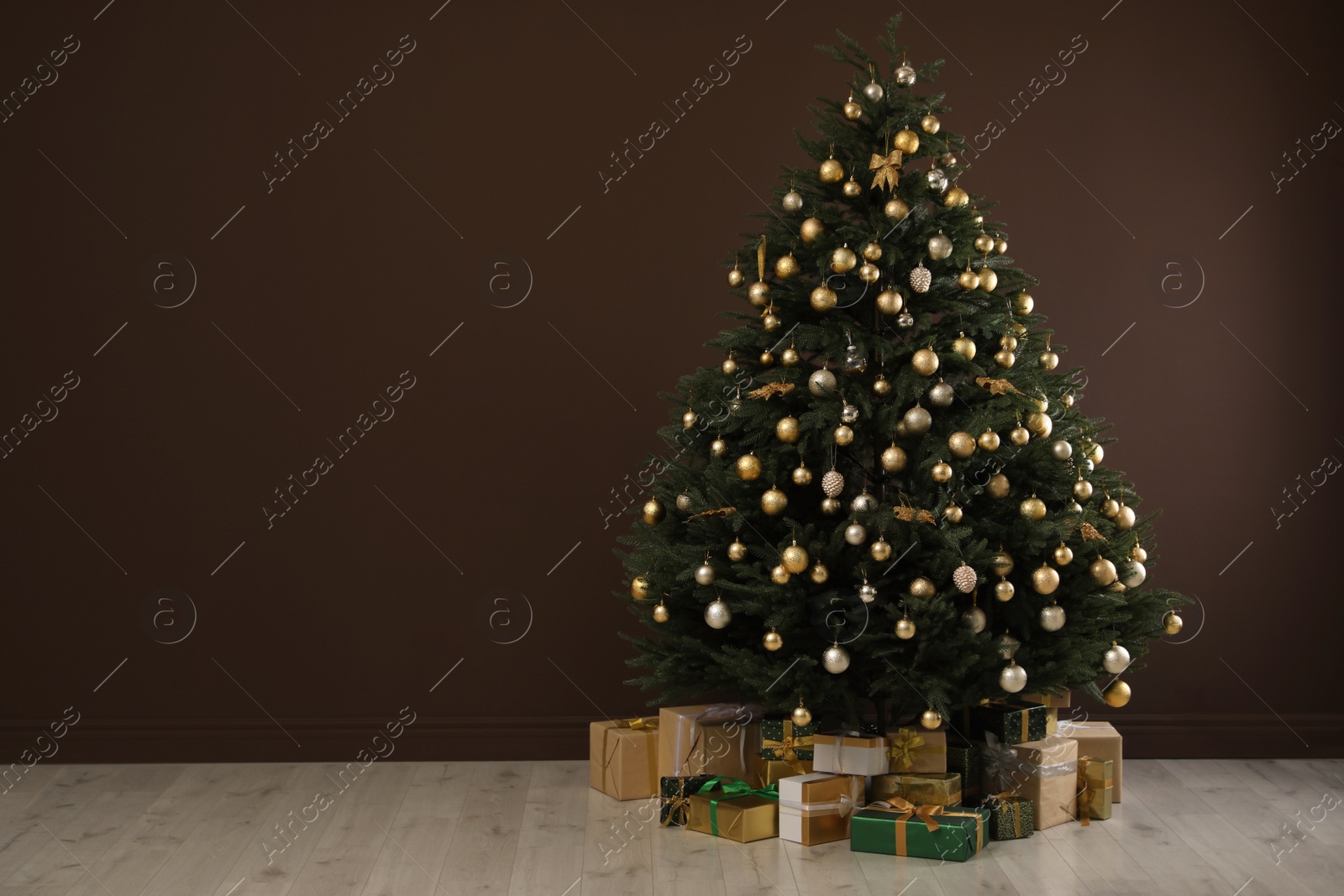 Photo of Beautifully decorated Christmas tree and many gift boxes near brown wall indoors, space for text