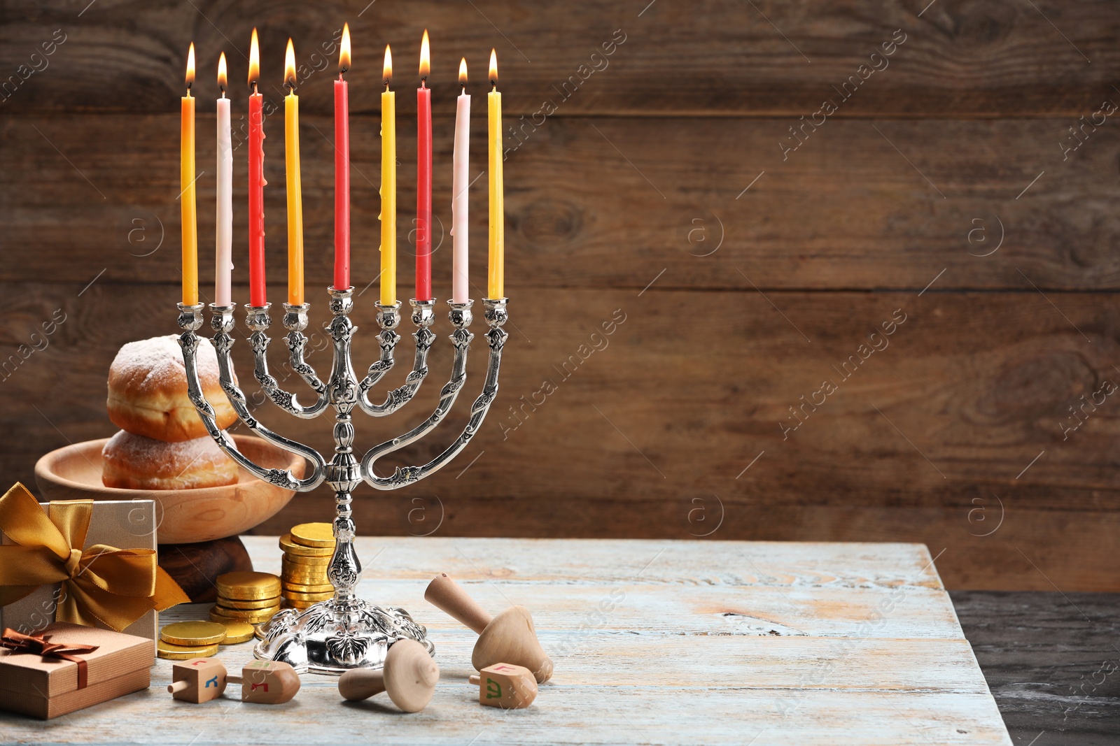 Photo of Hanukkah celebration. Menorah with burning candles, dreidels, donuts and gift boxes on wooden table, space for text