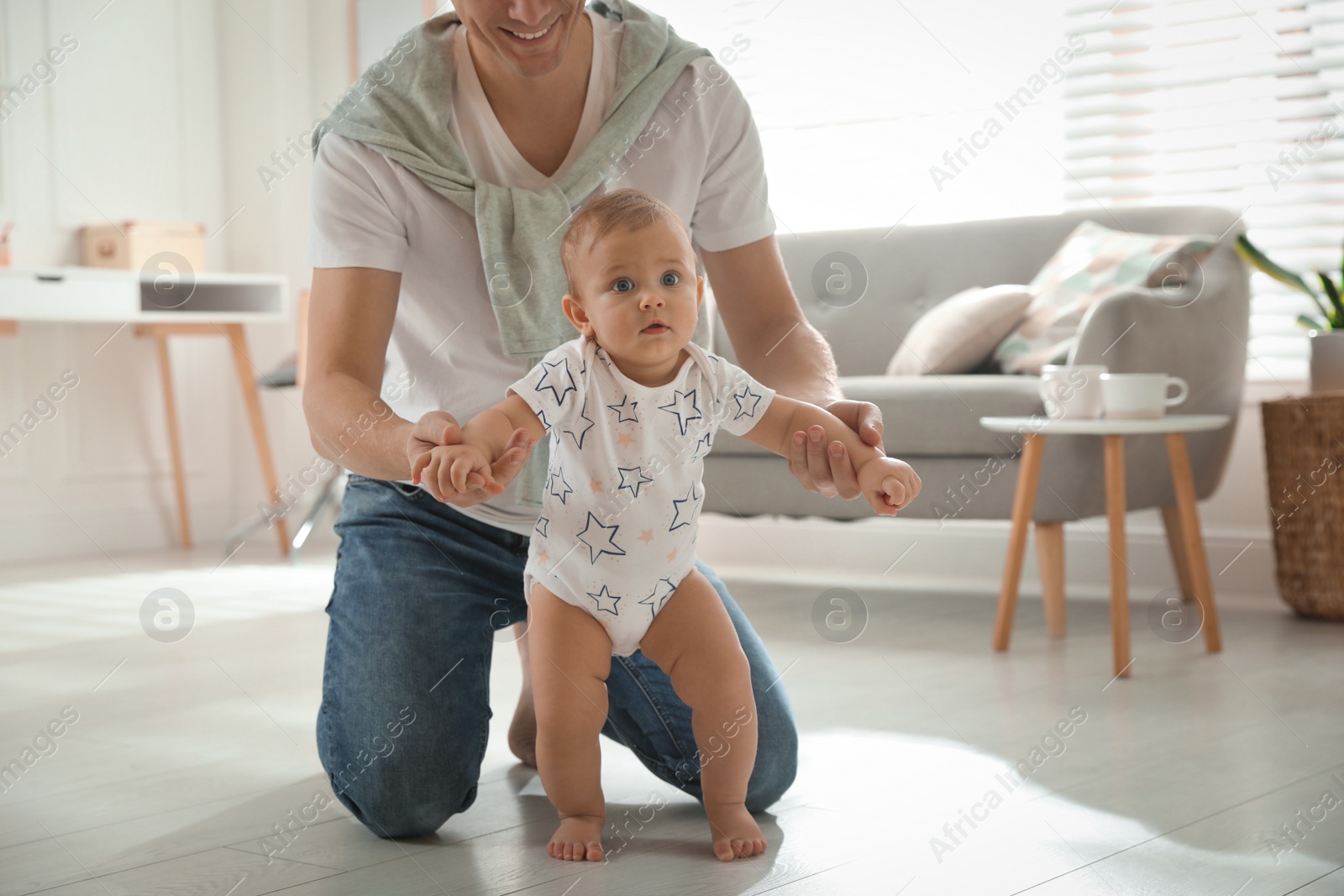 Photo of Father supporting his baby daughter while she learning to walk at home