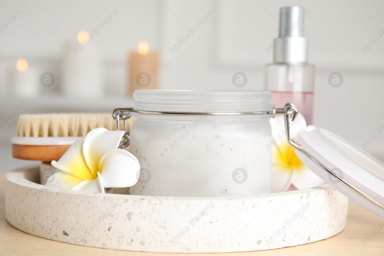 Photo of Jar of salt scrub and plumeria flowers on wooden table