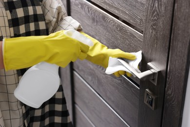 Woman cleaning door handle with detergent and paper towel, closeup