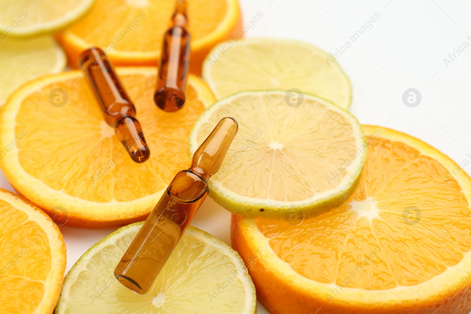 Photo of Skincare ampoules with vitamin C, lemon and orange slices on white background, closeup