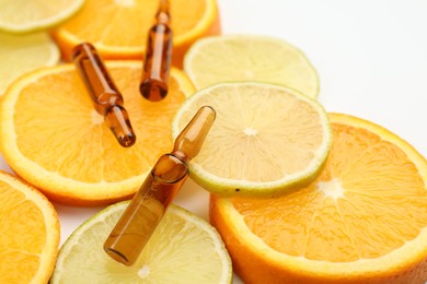 Skincare ampoules with vitamin C, lemon and orange slices on white background, closeup