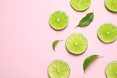 Photo of Juicy fresh lime slices and green leaves on pink background, flat lay. Space for text