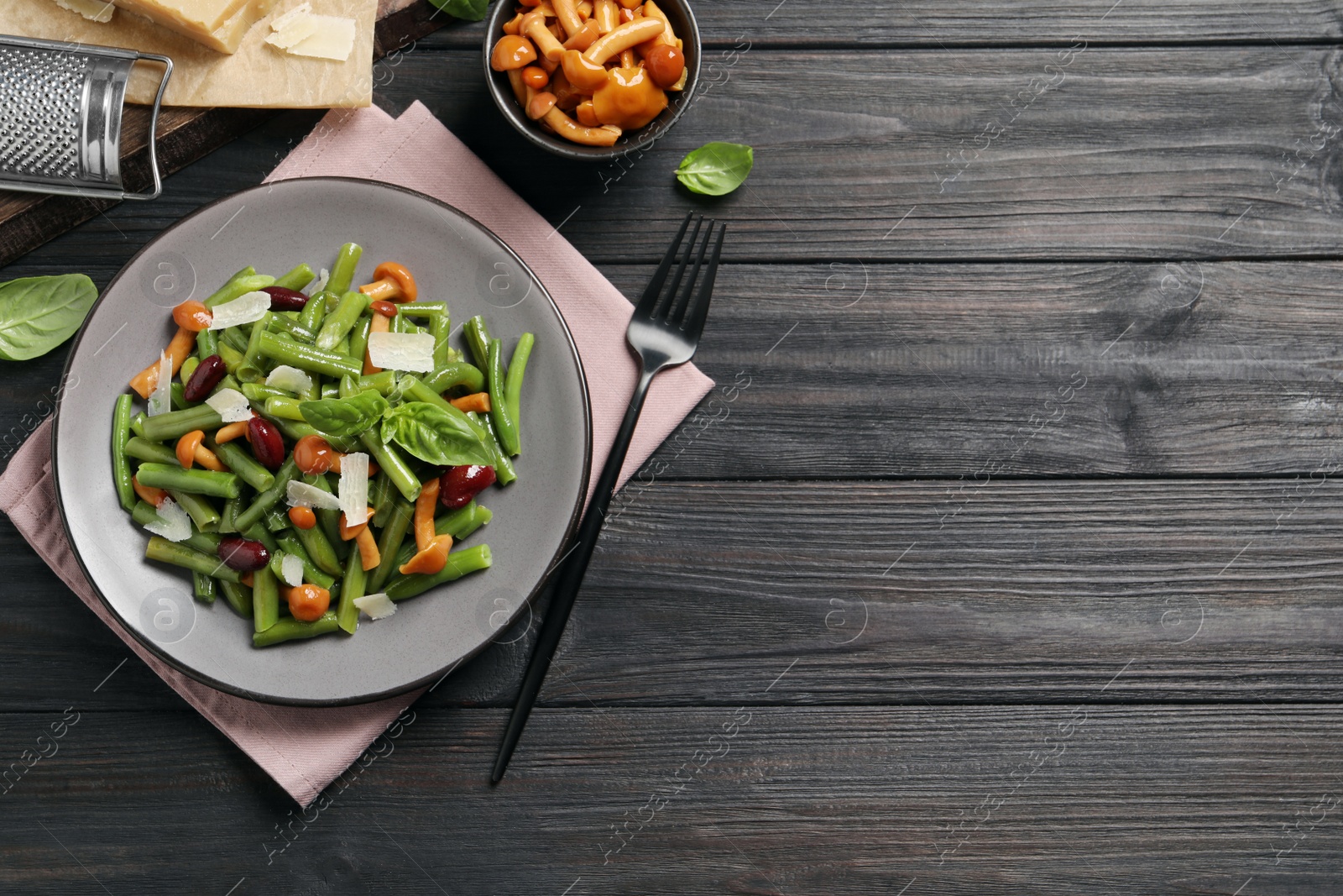Photo of Delicious salad with green beans, mushrooms and cheese served on black wooden table, flat lay. Space for text