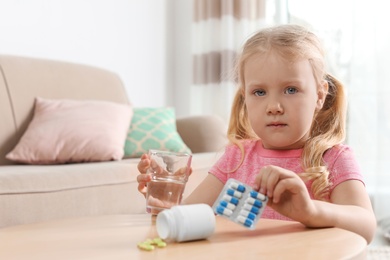 Little child with pills and water at table indoors, space for text. Danger of medicament intoxication
