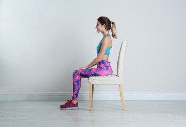 Photo of Young woman resting in chair after sports training near white wall. Home fitness