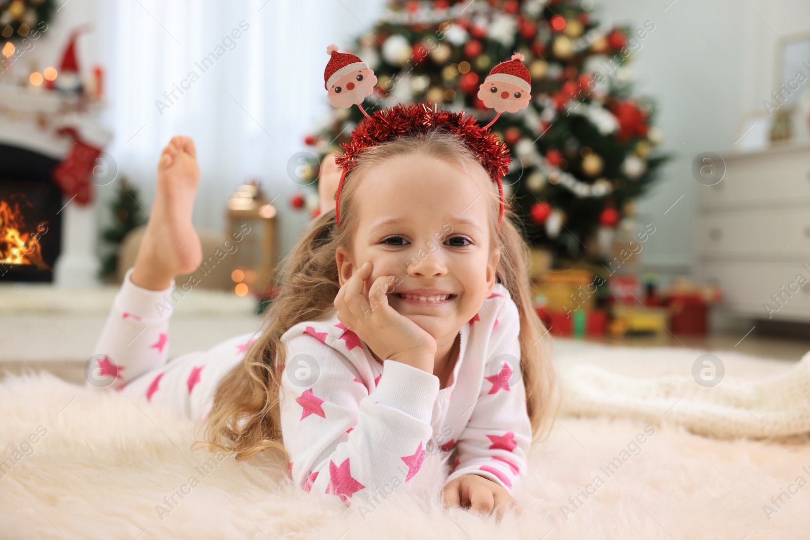 Photo of Cute little girl with festive headband in room decorated for Christmas