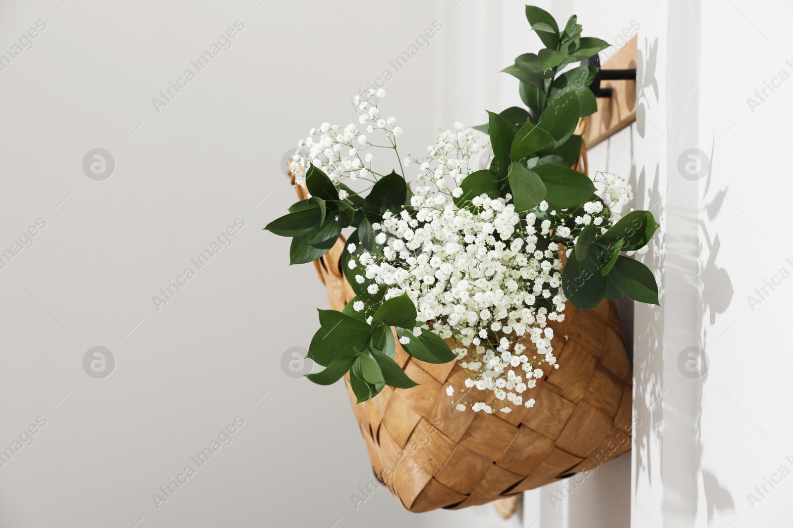 Photo of Stylish wicker basket with bouquet of flowers hanging on wooden rack indoors, space for text