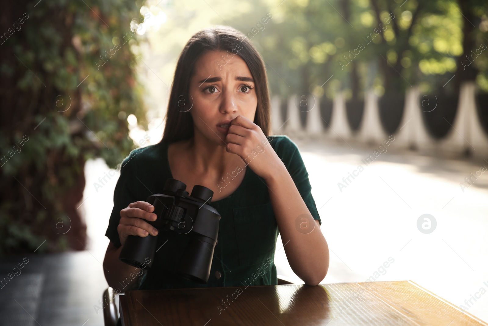 Photo of Jealous woman with binoculars spying on ex boyfriend in outdoor cafe