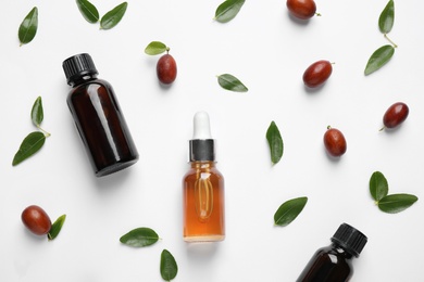 Photo of Glass bottles with jojoba oil and seeds on white background, top view