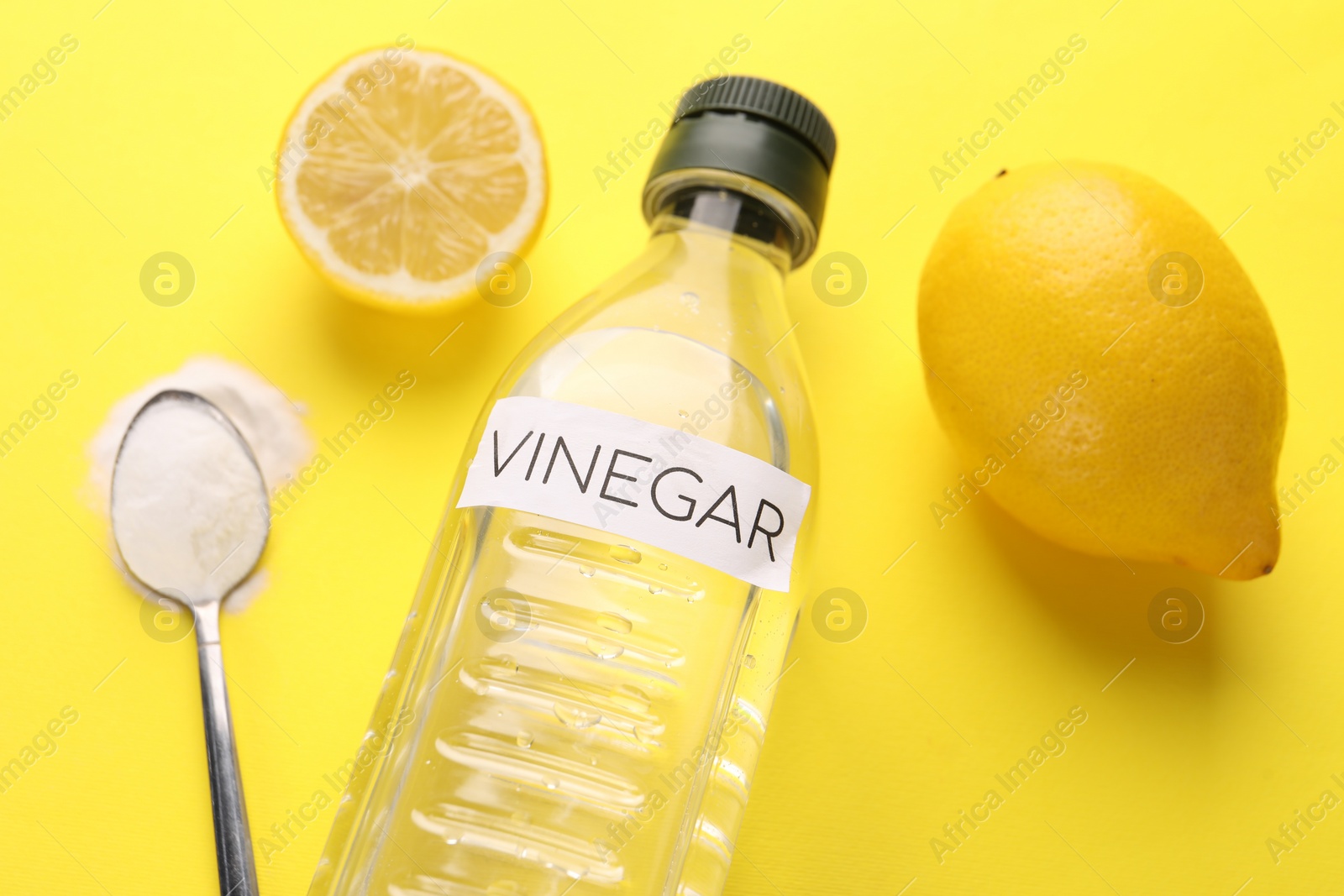 Photo of Eco friendly natural cleaners. Vinegar in bottle, lemons and spoon of soda on yellow background