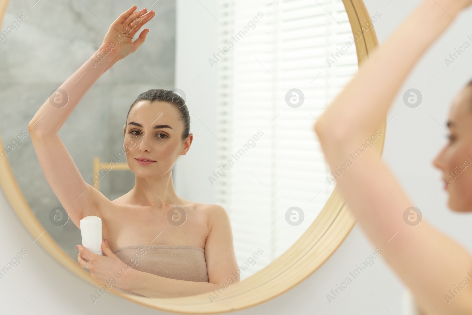 Photo of Beautiful woman applying deodorant near mirror in bathroom