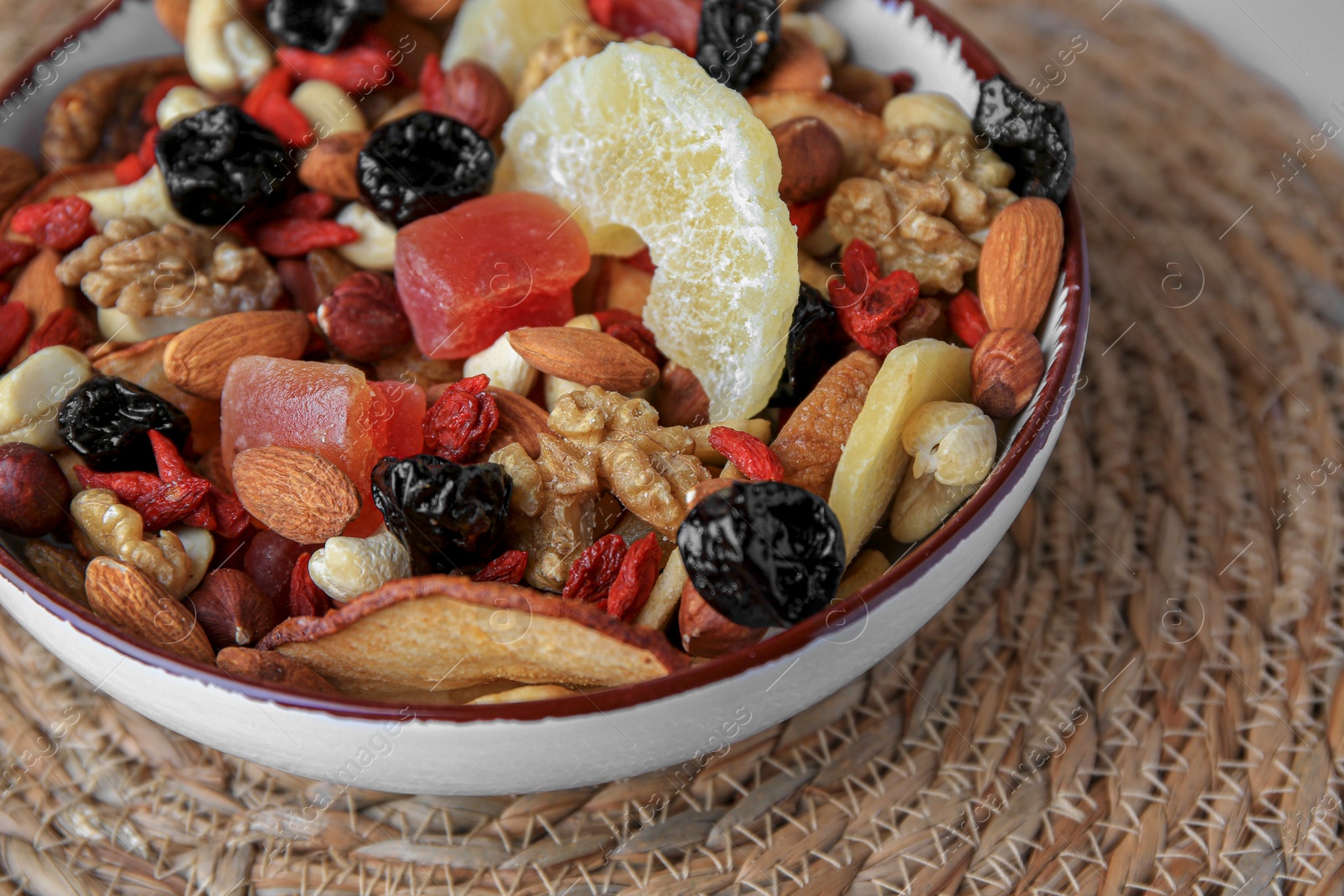 Photo of Bowl with mixed dried fruits and nuts on wicker mat, closeup