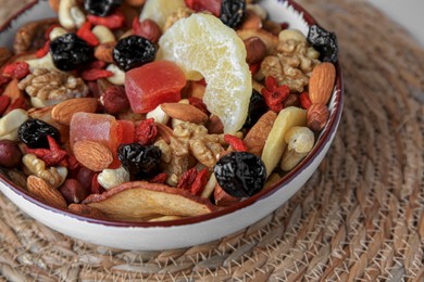 Photo of Bowl with mixed dried fruits and nuts on wicker mat, closeup