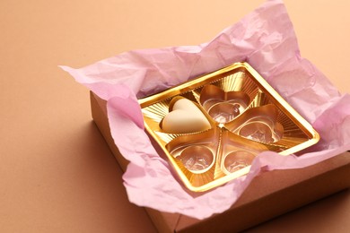 Photo of One heart shaped chocolate candy in box on light brown background. Space for text