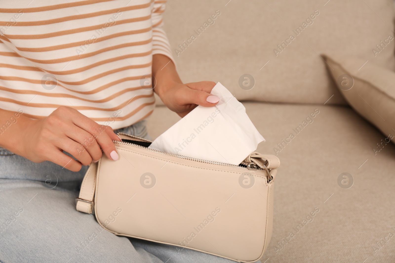 Photo of Woman putting disposable menstrual pad into purse at home, closeup