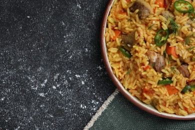 Photo of Delicious pilaf with meat on black textured table, top view. Space for text