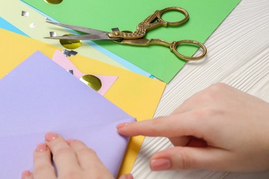 Woman with violet paper and scissors at white wooden table, closeup