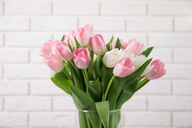 Photo of Beautiful bouquet of tulips in glass vase against white brick wall