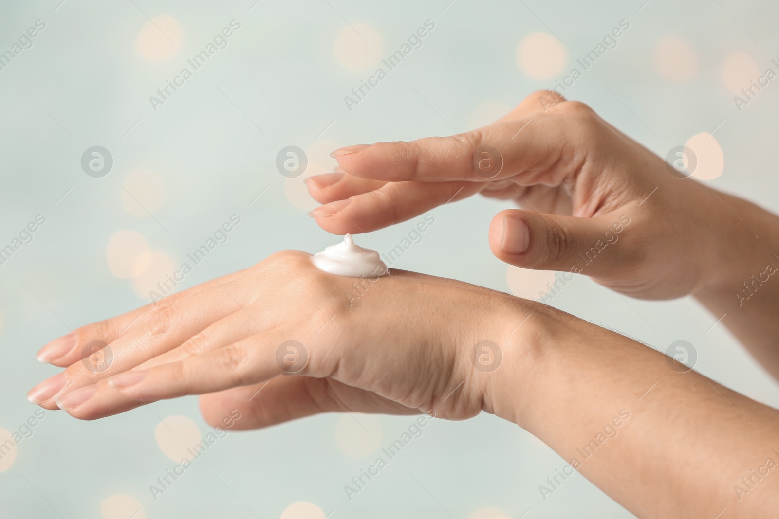 Photo of Woman applying hand cream on blurred background, closeup