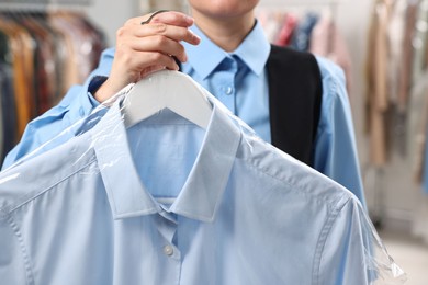 Dry-cleaning service. Woman holding shirt in plastic bag indoors, closeup