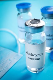 Monkeypox vaccine in glass vials and medical mask on light blue background