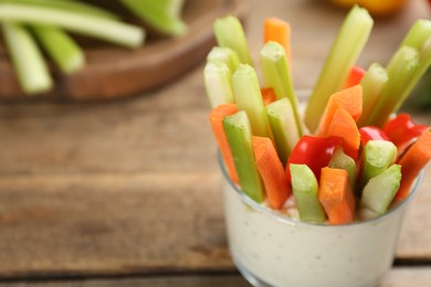 Celery and other vegetable sticks with dip sauce in glass bowl on wooden table, closeup. Space for text
