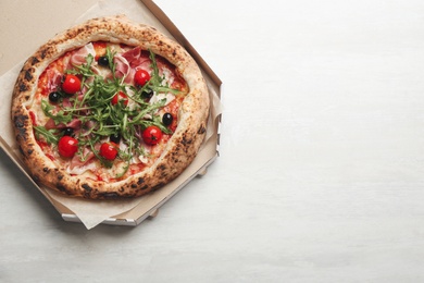 Photo of Tasty pizza with meat and arugula in cardboard box on white table, top view. Space for text