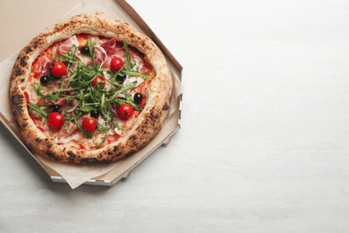 Tasty pizza with meat and arugula in cardboard box on white table, top view. Space for text