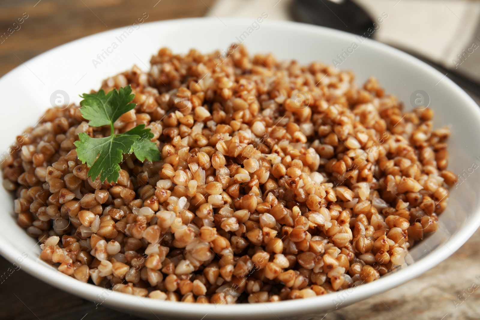 Photo of Bowl of buckwheat porridge with parsley on table, closeup