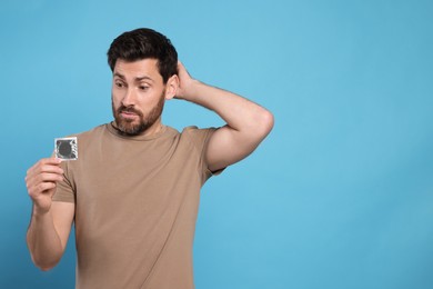 Photo of Confused man holding condom on light blue background, space for text. Safe sex