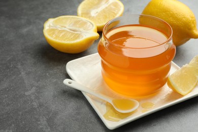 Photo of Sweet honey and fresh lemons on grey table, closeup. Space for text