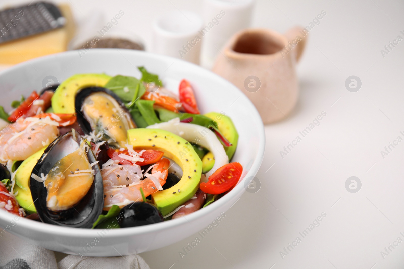 Photo of Bowl of delicious salad with seafood on white table, closeup. Space for text